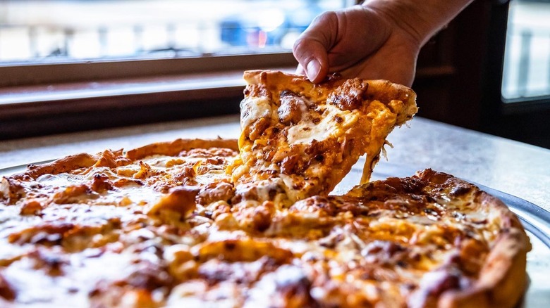 A person holding a slice of Golden BBQ Chicken pizza at Tilton House of pizza