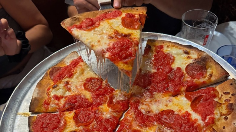 A person holding a piece of Pepperoni pizza at John's of Bleeker Street