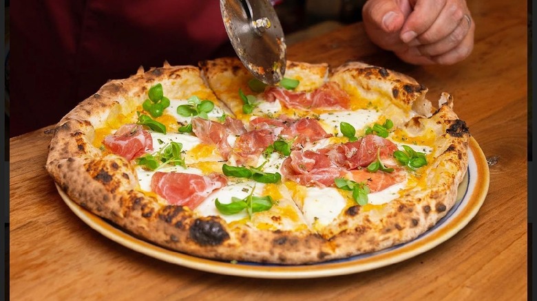 A person cutting a Nino Nanco pizza at Pasquale's Pizzeria Napoletana