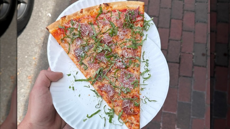 A person holding a slice of Prosciutto & Basil pizza at Five Points Pizza