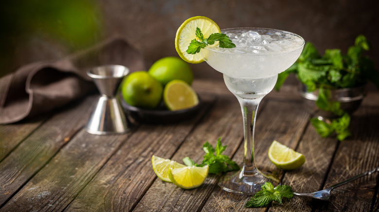 Margarita with mint leaves and lime wedges on a wooden table