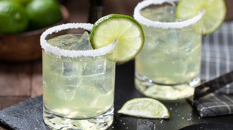 Two lime margaritas, surrounded by their ingredients, sit on a table