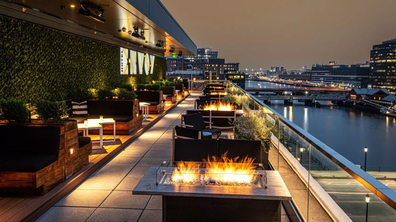 Outdoor patio of Rooftop at the Envoy in the evening with lit fire pits and views of the harbor and city