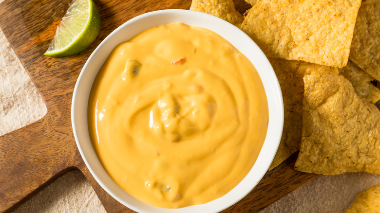 a bowl of queso dip, chips, and a lime slice