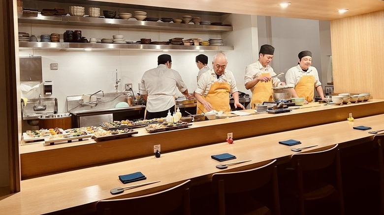 Shot of counter in front of kitchen, where chefs are preparing dishes