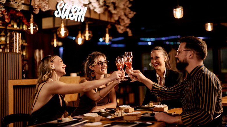 Group of friends toasting wine glasses at a sushi restaurant