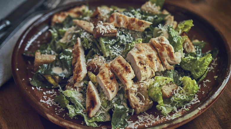 Chicken Caesar salad on a brown stoneware plate.