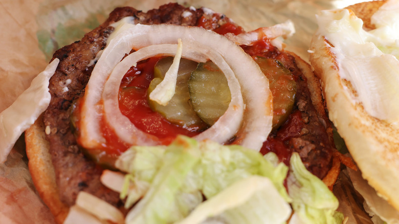 Whopper with the top bun off, showing onion slices, lettuce, pickles, ketchup, and the burger patty