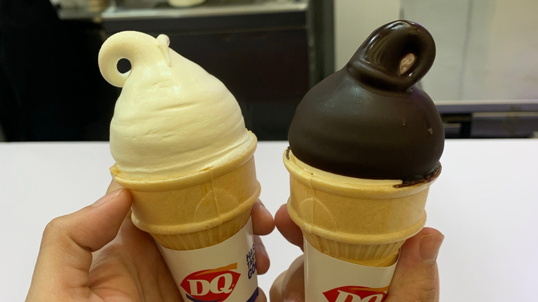 Two Dairy Queen ice cream cones held side by side, with one plain vanilla and the other with a chocolate hardshell topping