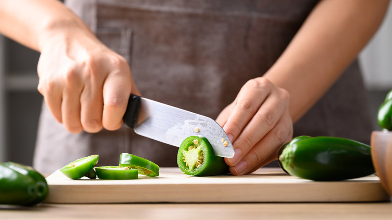 Person slicing a jalapeño with a chef's knife on a chopping board