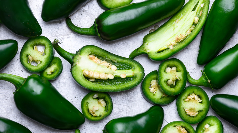 Whole, half and sliced green jalapeno hot peppers on metal sheet close up