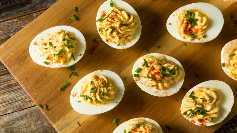 Deviled eggs topped with paprika and herbs on a wooden board