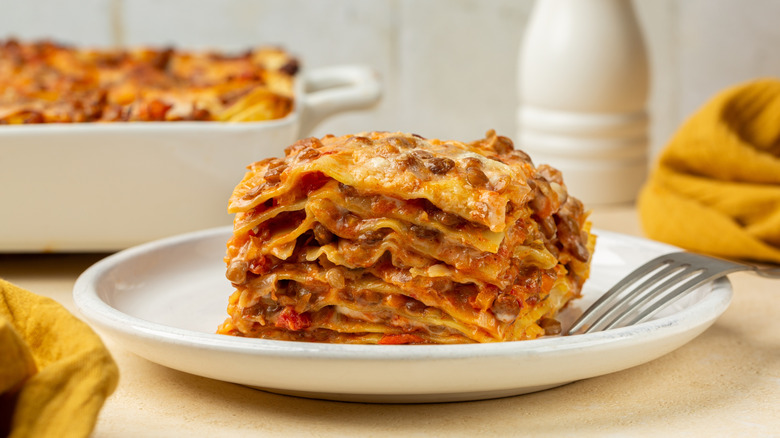 Close up of slice of homemade Red Lentil Lasagne in a white plate with a fork.