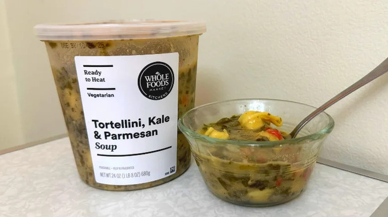 A tub of Whole Foods' Tortellini, Kale & Parmesan soup next to a small bowl filled with the soup