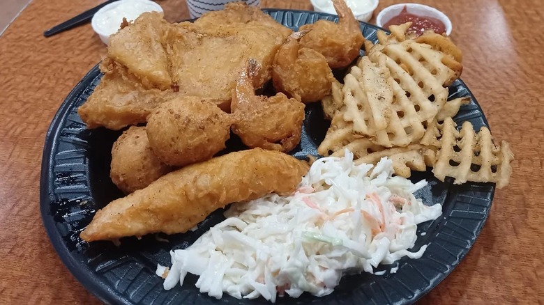 A sampler platter with fish, shrimp, chicken, waffle fries, and cole slaw served on black plate at Long John Silver's