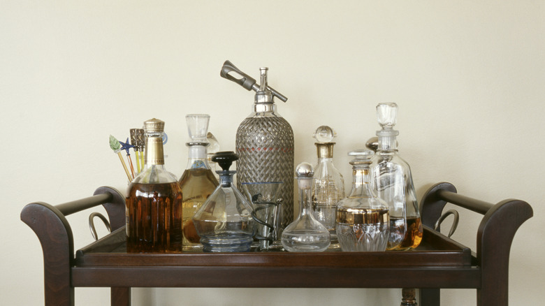 A bar cart is topped with an assortment of vintage-looking bottles