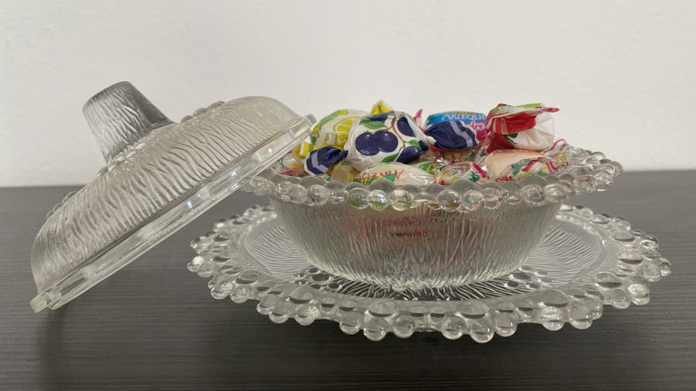 A pretty, clear, glass candy dish is filled with wrapped hard candies