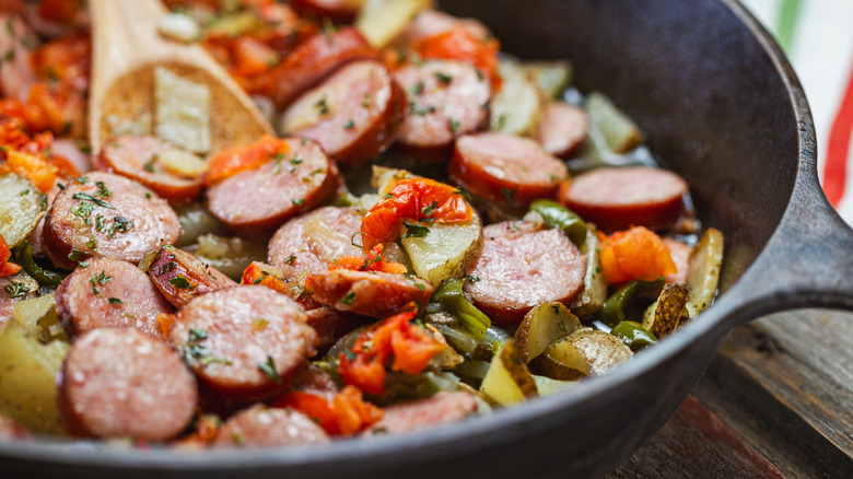 Cooking kielbasa in pan with vegetables.