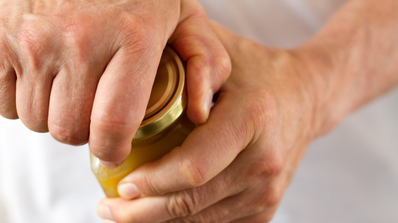 Close-up shot of strong male hands twisting open a stubborn jar lid.