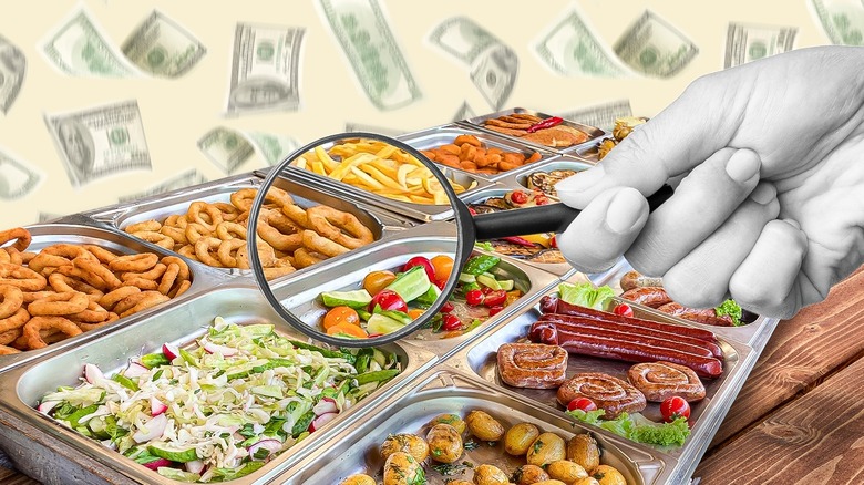 A large hand with a magnifying glass held over trays of buffet food