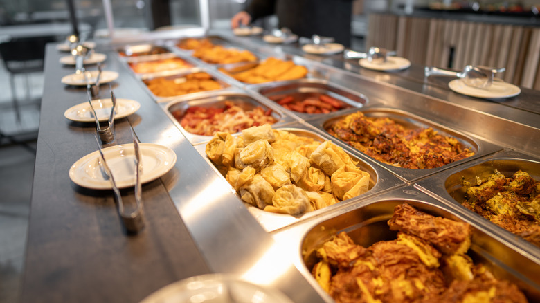 Different buffet food options with plates and tongs lined up in front