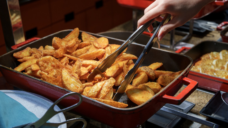Someone using tongs to help themselves to potato wedges at the buffet