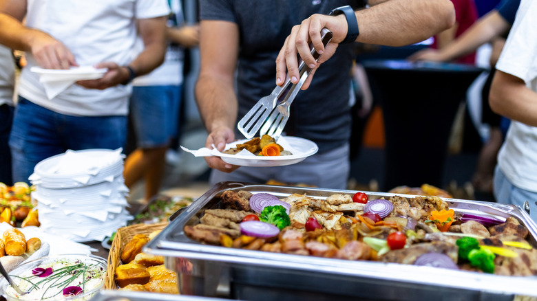 People waiting for the buffet while one person loads up their plate
