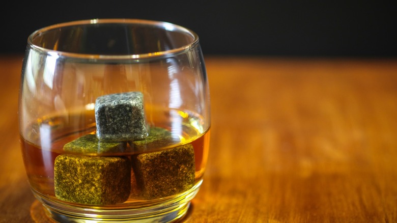 A glass of whiskey with three whiskey stones in it sitting on a table.