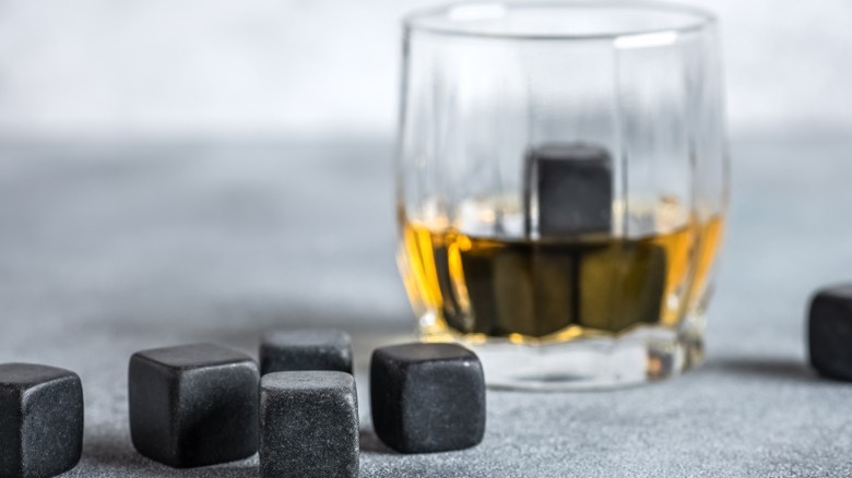 Black whiskey stones sitting around a whiskey glass with a few stones in it.