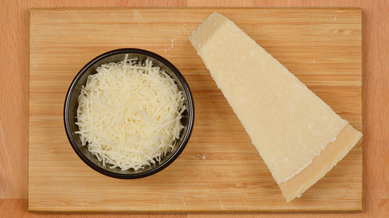 A Parmesan wedge next to grated Parmesan on a wooden board.