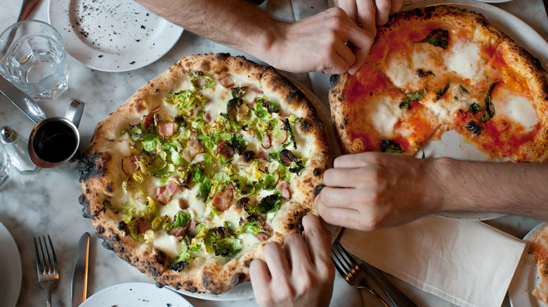 People at dinner table reaching for pizza