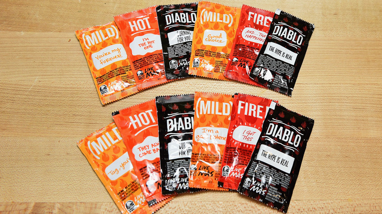 Taco Bell hot sauce packets spread out on a wooden surface