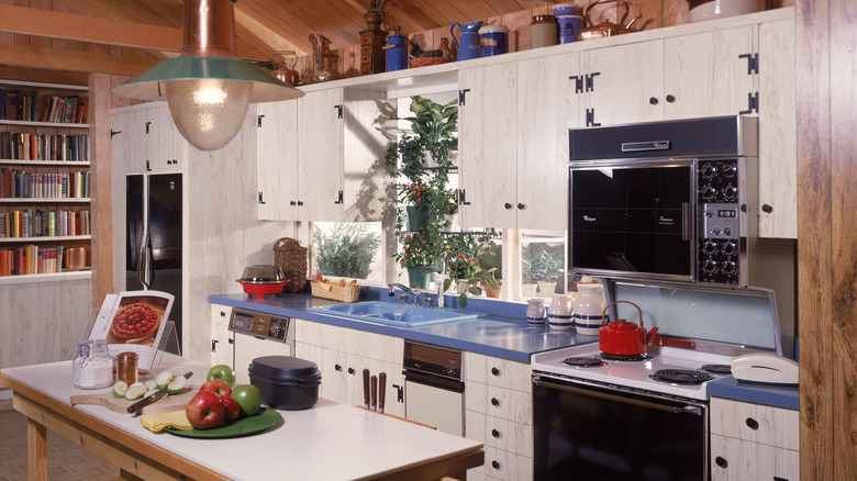 1980s kitchen with white cabinets, wood-paneled walls, and blue countertops.