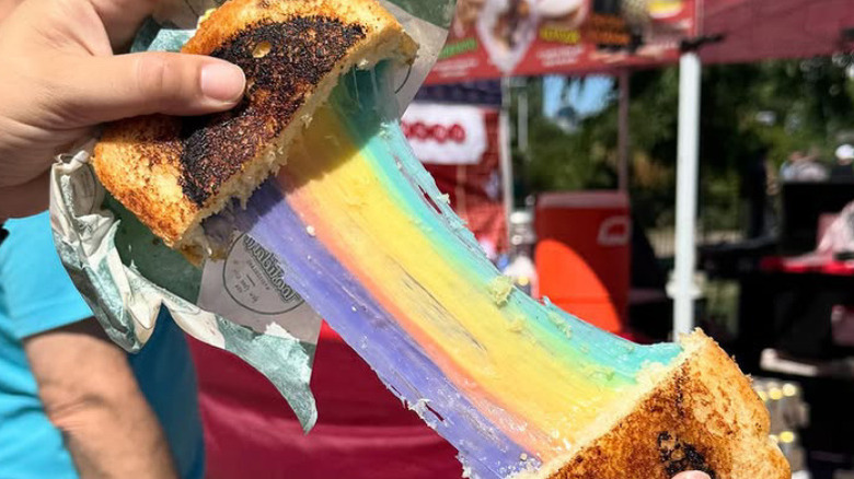 Toastieland rainbow sandwich held opened revealing rainbow cheese pull