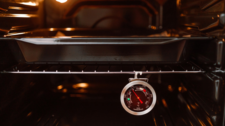 An oven thermometer hanging in an oven with a baking dish in it