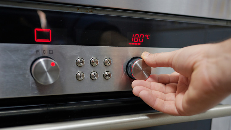 A hand adjusting a temperature knob on an oven