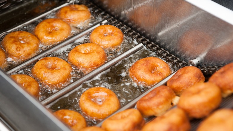 Golden donuts frying in deep fryer basket.