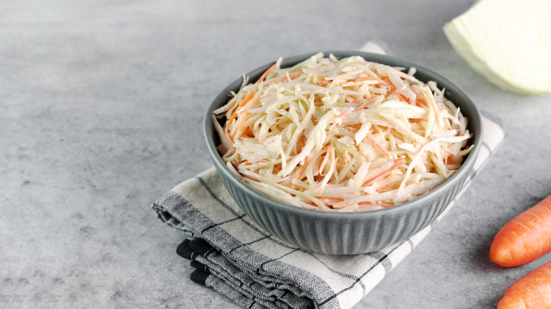 A bowl of coleslaw sits on a folded dish towel on a kitchen counter.