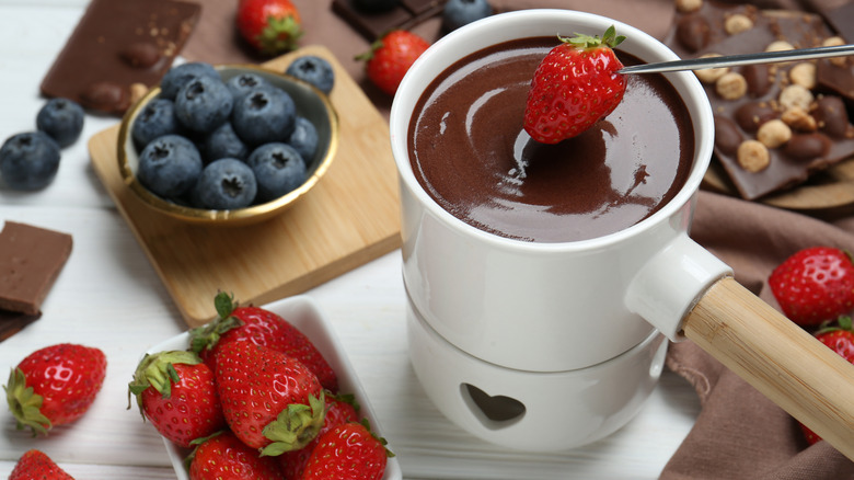 chocolate fondue with a strawberry being dipped in it and more berries on the side