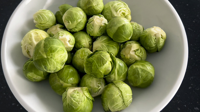 Raw brussels sprouts in a white bowl.
