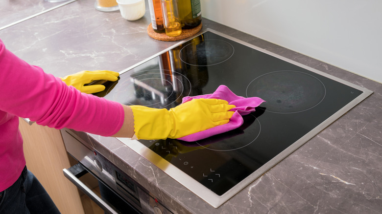 A pair of hands in rubber gloves cleaning a glass stovetop.