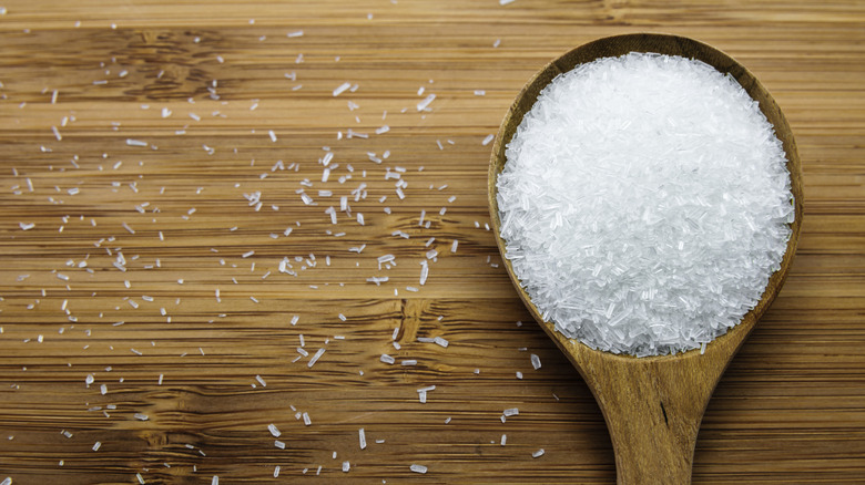 A wooden spoon full of MSG on a wooden board in close-up.