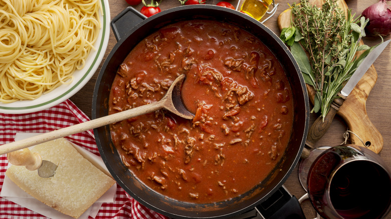 A pot of red sauce arranges around a bowl of plain spaghetti, a Parm wedge, herbs, and other ingredients.
