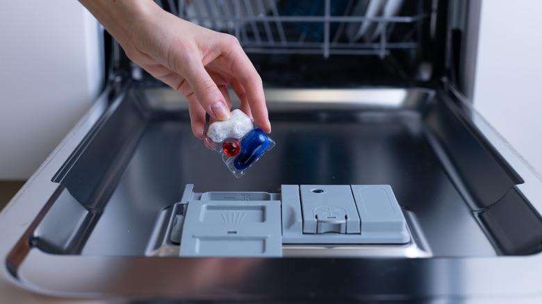 A hand places a detergent pod into a dishwasher.