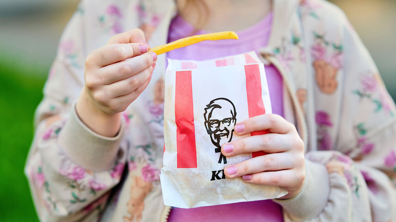 A woman eats fries from a KFC bag