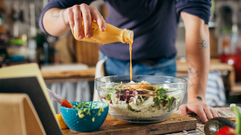 Person pouring dressing onto a salad