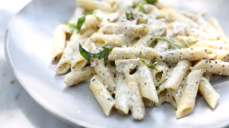 Penne rigate on a white plate with white sauce, pepper, and herbs