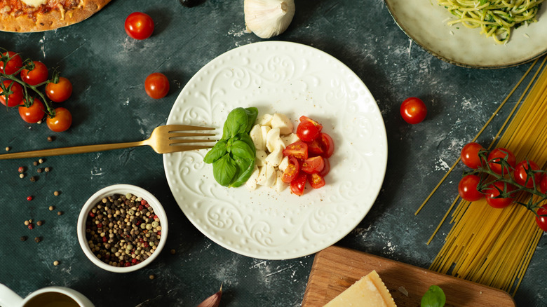 A plate with tomatoes, cheese, and basil as well as a fork
