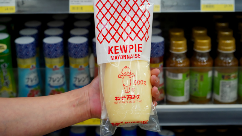 Close up of Japanese style Kewpie brand mayonnaise held in hand in a local supermarket aisle with product labels visible in the background.