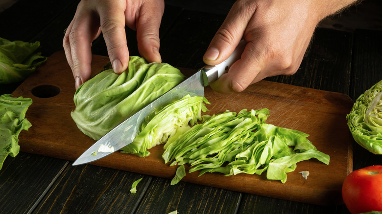 A person's hands are seen chopping cabbage on a cutting board.